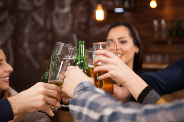 Happy young friends clinking beer bottles in vintage old styled pub