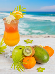 Summer cocktail with various tropical fruits around. Apple, kiwi, tangerine, orange, mango, carambola.