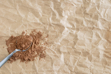 Metal teaspoon with dry cocoa powder. On crumpled brown paper background.