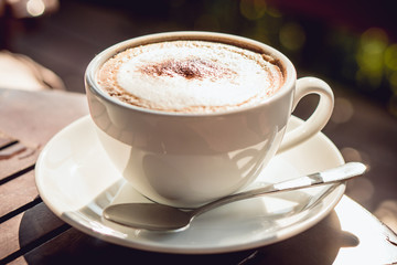 Hot coffee place on the wooden table in early morning, white cup and silver spoon.