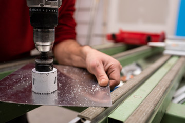 worker cutting a hole on aluminium plate with a crown drill