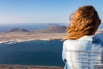 Fototapeta premium A woman stands on the edge of a cliff and looks at a nearby island in the ocean.