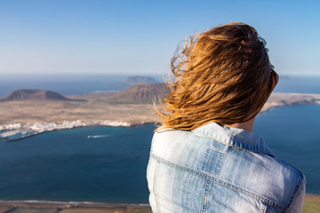 Fototapeta na wymiar A woman stands on the edge of a cliff and looks at a nearby island in the ocean.