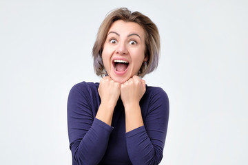 Cheerful, charming, pretty woman with wide open mouth, holding palms near face