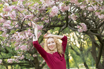 girl the blonde. girl near cherry blossoms. It's spring. cherry blossoms. the girl in the Burgundy dress. Sakura on twilight. portrait at sunset