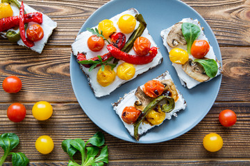 Delicious vegetarian sandwiches with grilled tomatoes, paprika and green on rustic table, top view. Colorful food. 