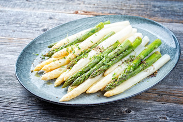 Traditional boiled white and green asparagus with butter sauce decorated with cress as closeup on a design plate on a wooden table