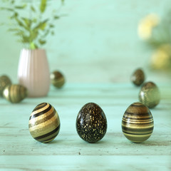 Three golden and black easter eggs on mint green background
