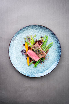 Traditional barbecue aged venison backstrap roast with green asparagus, carrots and herbs in brown red wine sauce as top view on a modern design plate with copy space