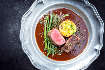 Traditional barbecue aged venison backstrap roast with green beans, fried mashed potatoes and herbs in brown red wine sauce as top view on a pewter plate with copy space