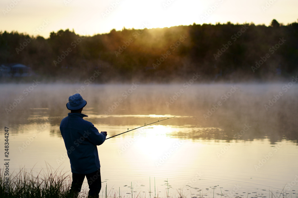 Wall mural caucasian fisherman, 50's, at the lake with fog, early morning just before sunrise.