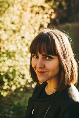 Smiling young woman looking at the camera. Happy caucasian girl against autumn bushes in the botanical garden. Beautiful blue eyes. 