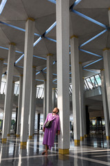 A male tourist in the nationally mosque of the city of Kuala Lumpur stands near the column and enjoys the beauty of the interior.