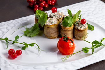 Eggplant rolls with a filling, on a white plate of urshenoy baked tomato. Dark background decorated with vegetables and viburnum