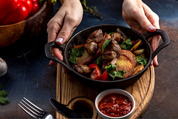 Frying pan with roast beef and potatoes, roasted vegetables and greens, on a light board on a black background. The background is decorated with vegetables.
