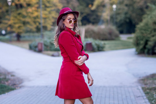 Sexy woman in red coat with red hat on her head and sunglasses in park standing