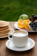 Healthy breakfast. Deliciouse homemade american pancakes with cup of coffee and fruits. Wooden table, beautiful morning in garden.