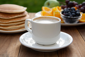 Healthy breakfast. Deliciouse homemade american pancakes with cup of coffee and fruits. Wooden table, beautiful morning in garden.