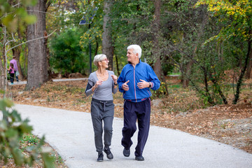 Obraz premium Active senior couple jogging in the park at autumng day and smile