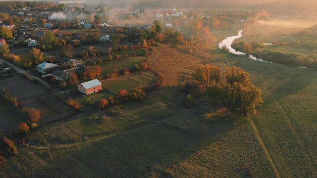 Aerial fly above countryside river with domestic birds at sunrise - sunset in autumn smoke, 4K