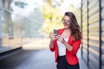 Long hair beautiful business woman in red suit reading text message on mobile phone