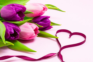 Heart shape made of purple ribbon and bouquet of purple and pink tulips on a light pink background. Valentines Day, 8 March, Mother and Women's Day concept.