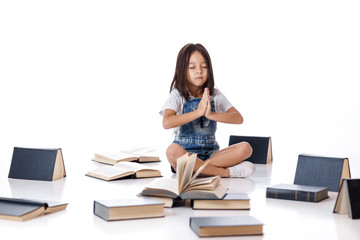 cute little girl in denim sitting in a lotus position between books on white background. child and a lot of books. Children and education.