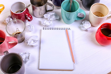 Empty dirty coffee cups, different colors on the table and a notebook for writing a letter. Concept caffeine dope, lack of energy to solve the problem. Copy space.