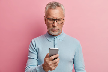 Serious mature man focused in screen of smartphone, connected to wireless internet, searches...