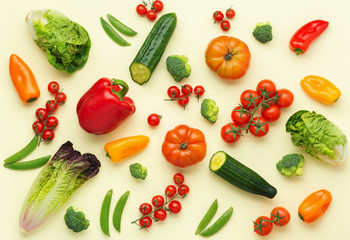 Fresh raw ingredients for salad tomatoes cucumbers lettuce pepper avocado spring onion broccoli peas on light yellow table, top view, selective focus