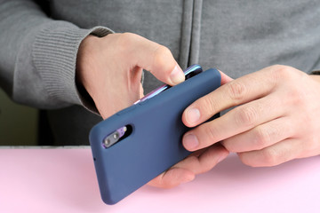 Caucasian man in a gray sweater puts on a new case on mobile phone with selective focus. White male hands are holding a smartphone and putting on a blue cover. Silicone case for digital gadget