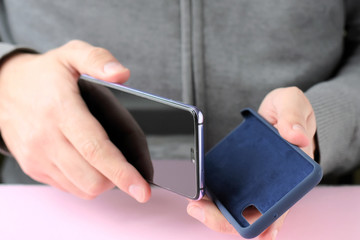 Caucasian man in a gray sweater puts on a new case on mobile phone with selective focus. White male...