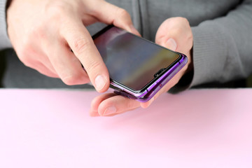 Male hands are holding a phone and putting on a shiny colorful cover. White man in a gray sweater put on a new violet case on smartphone with selective focus. Plastic case for digital gadget