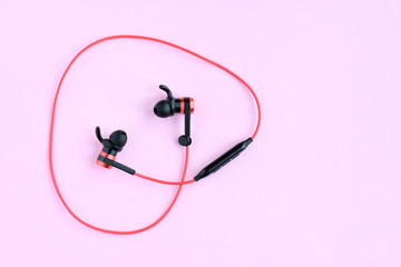 Wireless bluetooth red earphones with selective focus on neutral pink background. Smart digital...