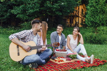 Two  beautiful girls with two boys sitting in a park on a blanket carpet  with guitar,they have picnic and listening melody of guitar