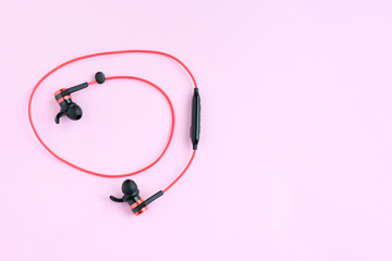 Wireless bluetooth red earphones with selective focus on neutral pink background. Smart digital...