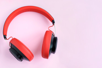 Red headphones with selective focus on pink background. Bluetooth red earphones. Smart digital sound personal headset. Mobile music stereo headphones. Wireless gadget for listening music