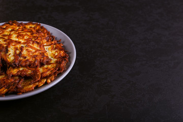 Hash brown and sour cream on a plate on a dark stone background, well fried. Copy space.