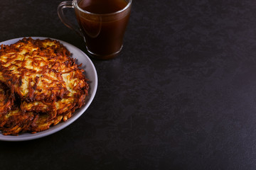 Hash brown and sour cream on a plate on a dark stone background, well fried. Copy space.