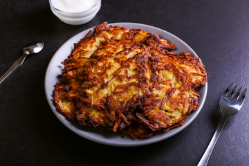 Hash brown and sour cream on a plate on a dark stone background, well fried. Copy space.