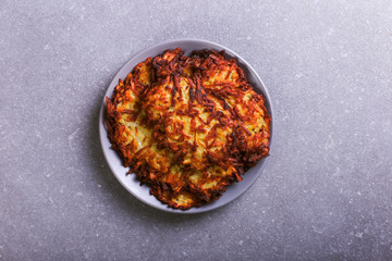 Hash brown and sour cream on a plate against a gray stone background, well fried. Copy space.