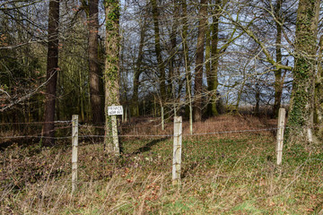 Woodland with "keep out" sign attached to a tree, and a fence in the foreground.