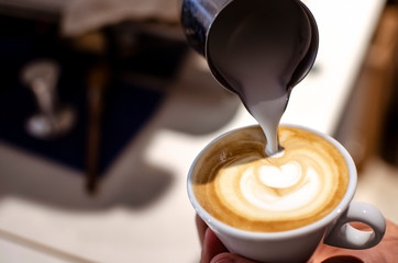 Pouring milk into espresso cup, making latte art with foam, closeup