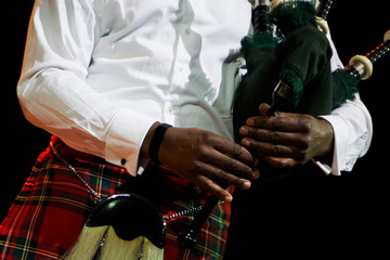 A black man in a white shirt and Scottish kilt holds bagpipes. Multicultural