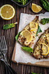 Baked pollock fillet with lemon and spinach on a wooden background