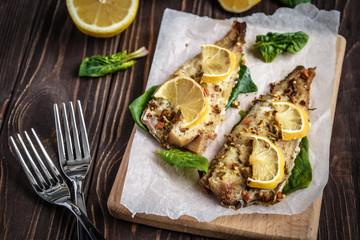 Baked pollock fillet with lemon and spinach on a wooden background