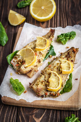 Baked pollock fillet with lemon and spinach on a wooden background