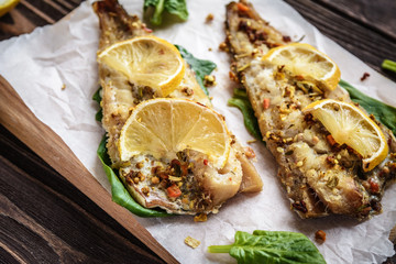 Baked pollock fillet with lemon and spinach on a wooden background