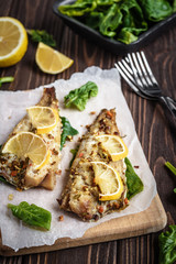 Baked pollock fillet with lemon and spinach on a wooden background
