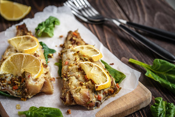 Baked pollock fillet with lemon and spinach on a wooden background